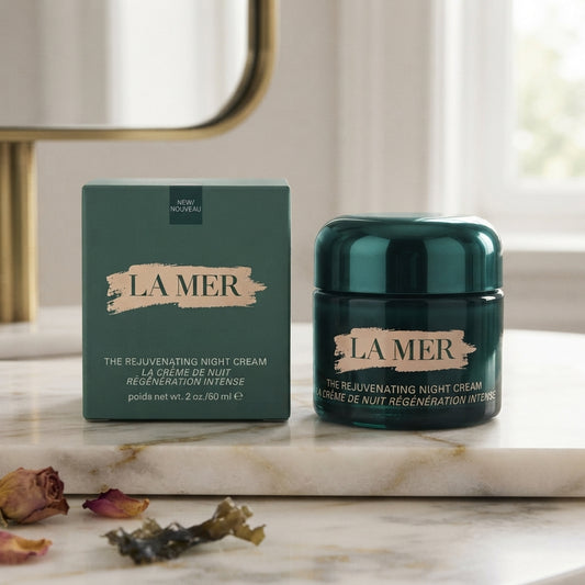 La Mer The Rejuvenating Night Cream 2 oz jar and its matching green packaging box, displayed on a marble surface with dried rose petals in the foreground.