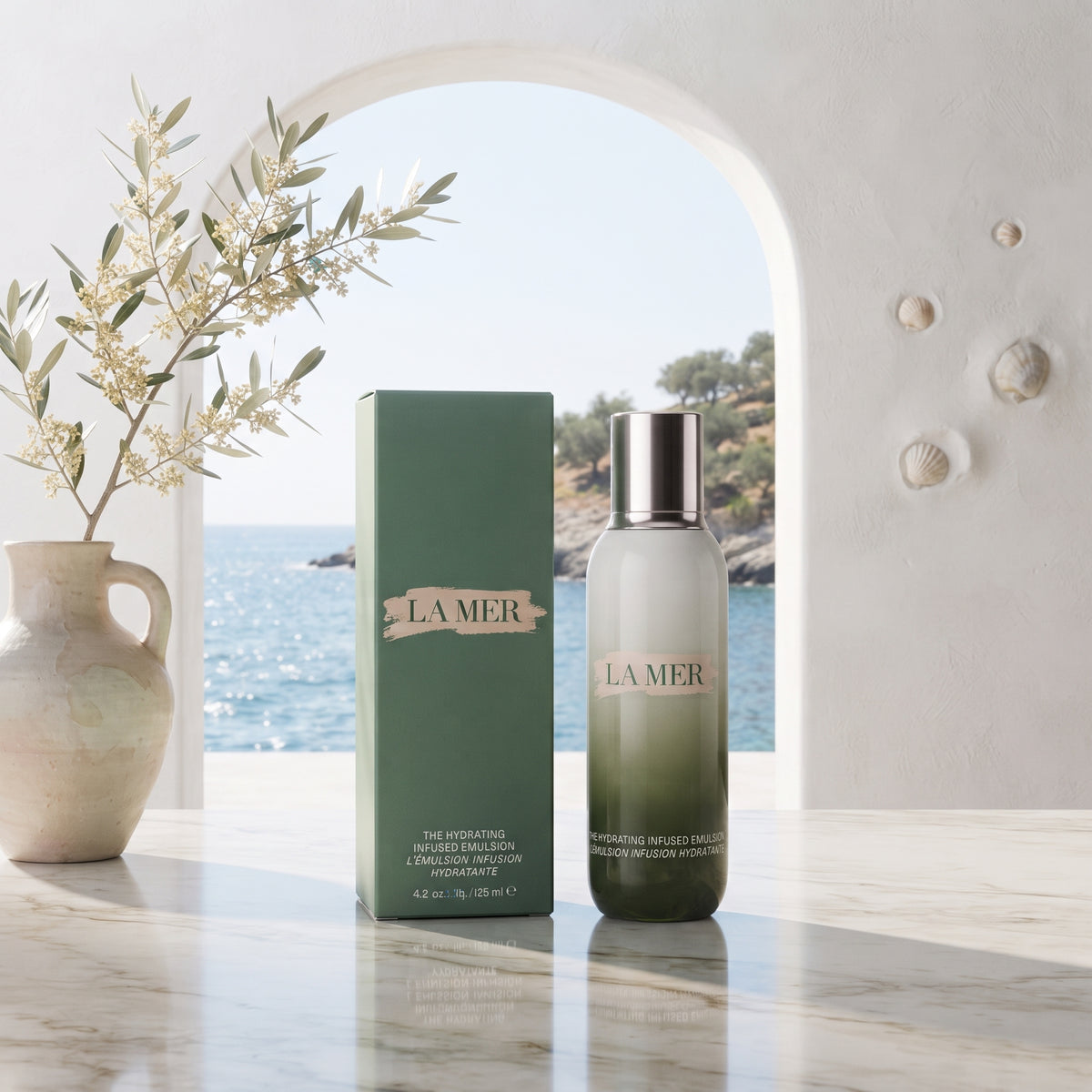 La Mer The Hydrated Skin Lotion bottle and its green box displayed on a marble surface, with a vase of branches and a sea-view window in the background.