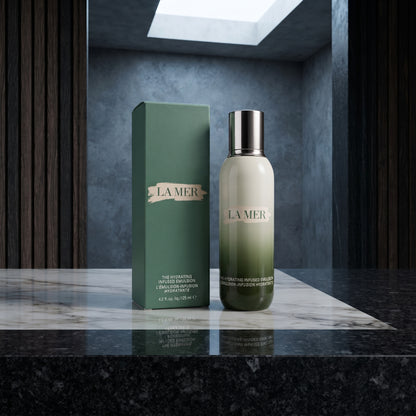 La Mer Hydrating Infused Treatment serum bottle with a silver cap standing next to its green box on a polished marble surface.